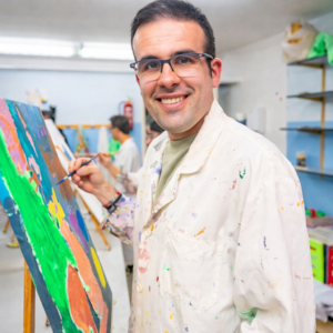 Male teacher in lab coat painting with students in art class, promoting inclusive education for autism.
